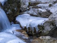 Dicke Eisfläche auf Felsen neben Bachkaskade